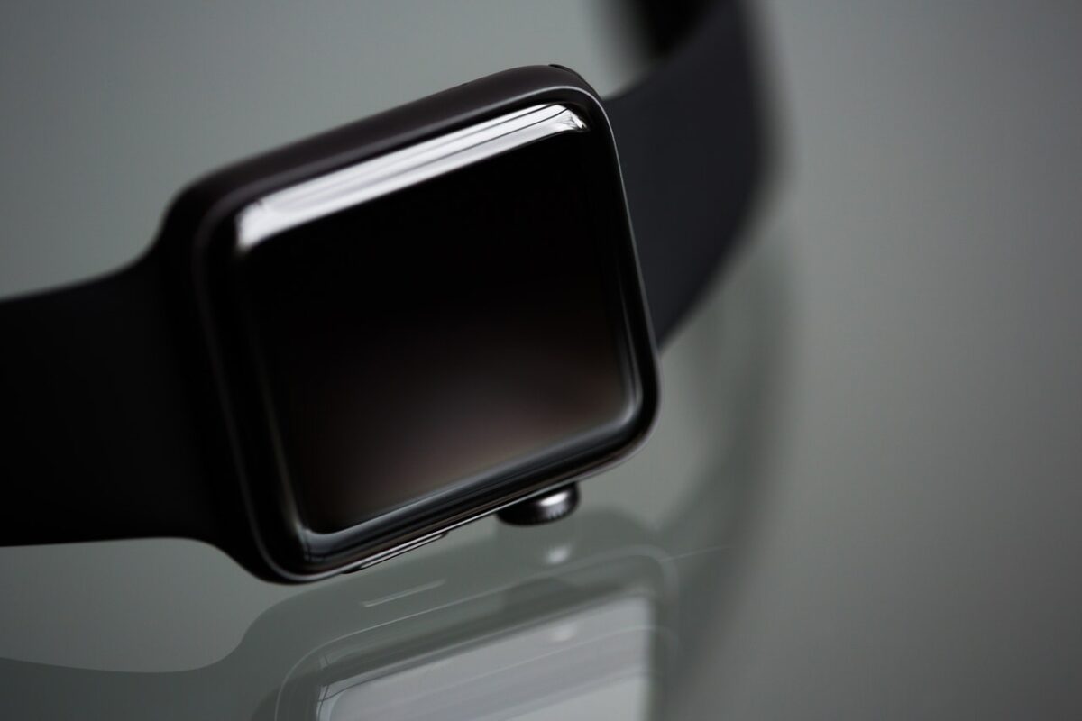 A close-up of a smartwatch with a sleek black design and a glossy screen, functioning as a fitness tracking device, reflecting softly on a dark, shiny surface.