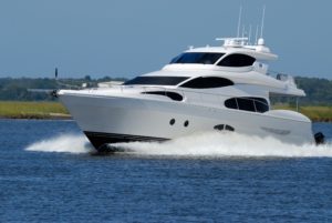 A luxury white yacht speeding through blue waters near a grassy coastline under a clear sky, with increased surveillance due to recent boat accidents in the area.