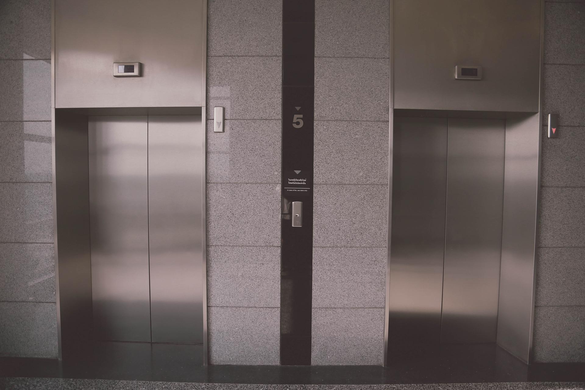 Three closed elevator doors on a gray tiled wall with a central call panel displaying the number 5, and emergency features indicated nearby to ensure safety against potential elevator accidents.