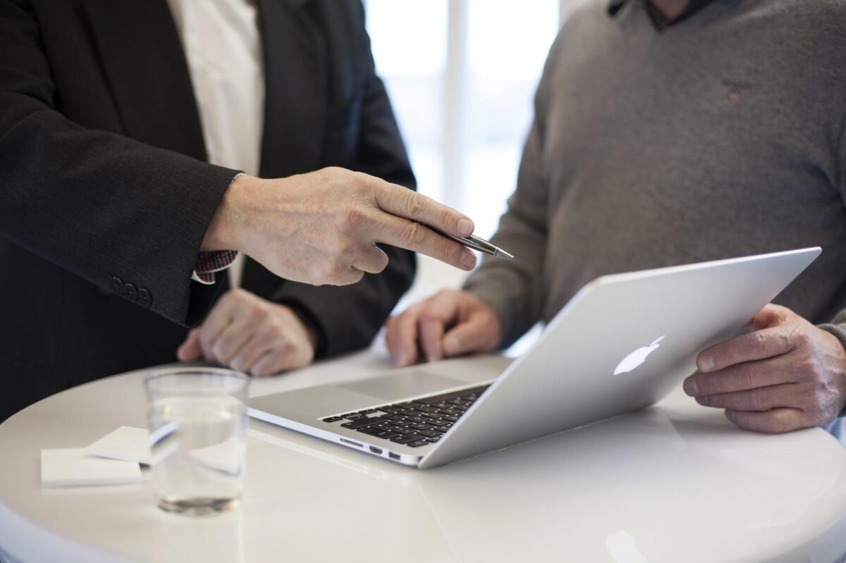 Two individuals in a personal injury consultation, one pointing at a laptop screen while discussing, with a glass of water and business cards on the table.