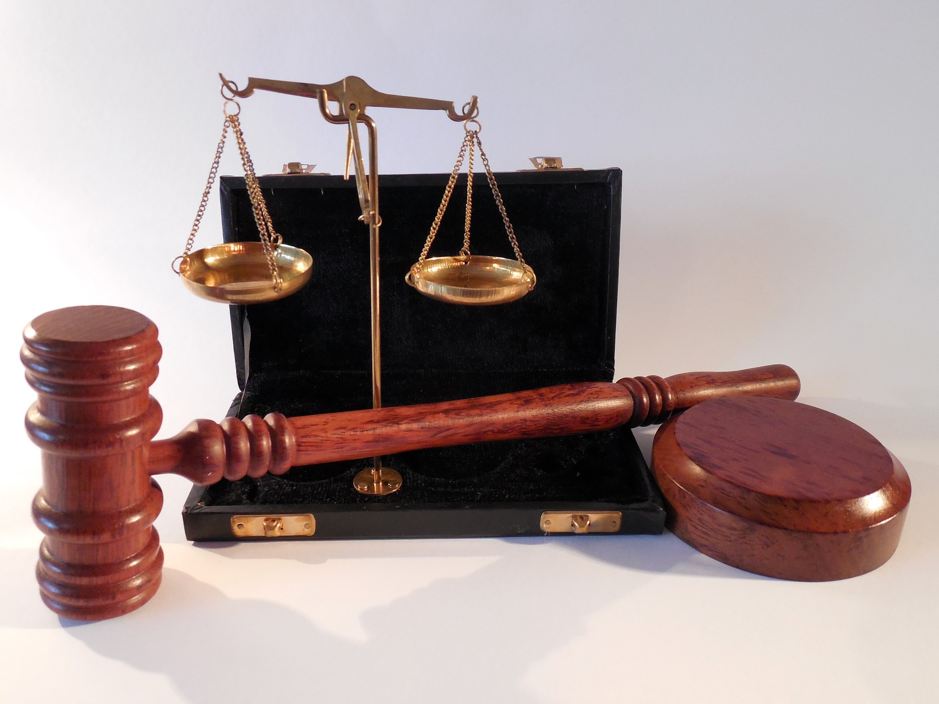 A wooden gavel rests beside a set of brass balance scales, integral to the court's solemn proceedings. Both are placed on a dark surface and housed in a black case with a white backdrop, symbolizing justice and the pursuit of personal injury claims.