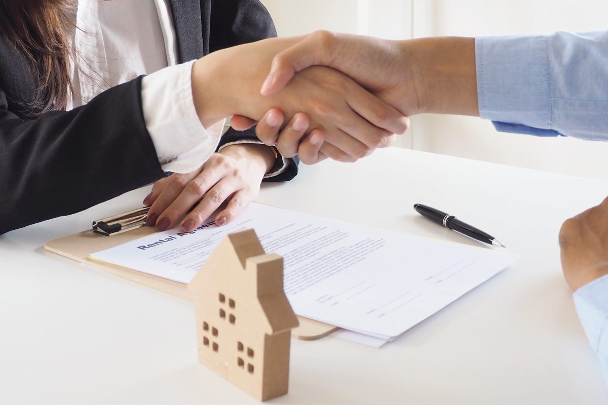 Two people shaking hands over a table with a house model and rental agreement documents, signified by Commercial Title Insurance Attorneys to represent a secured real estate deal.