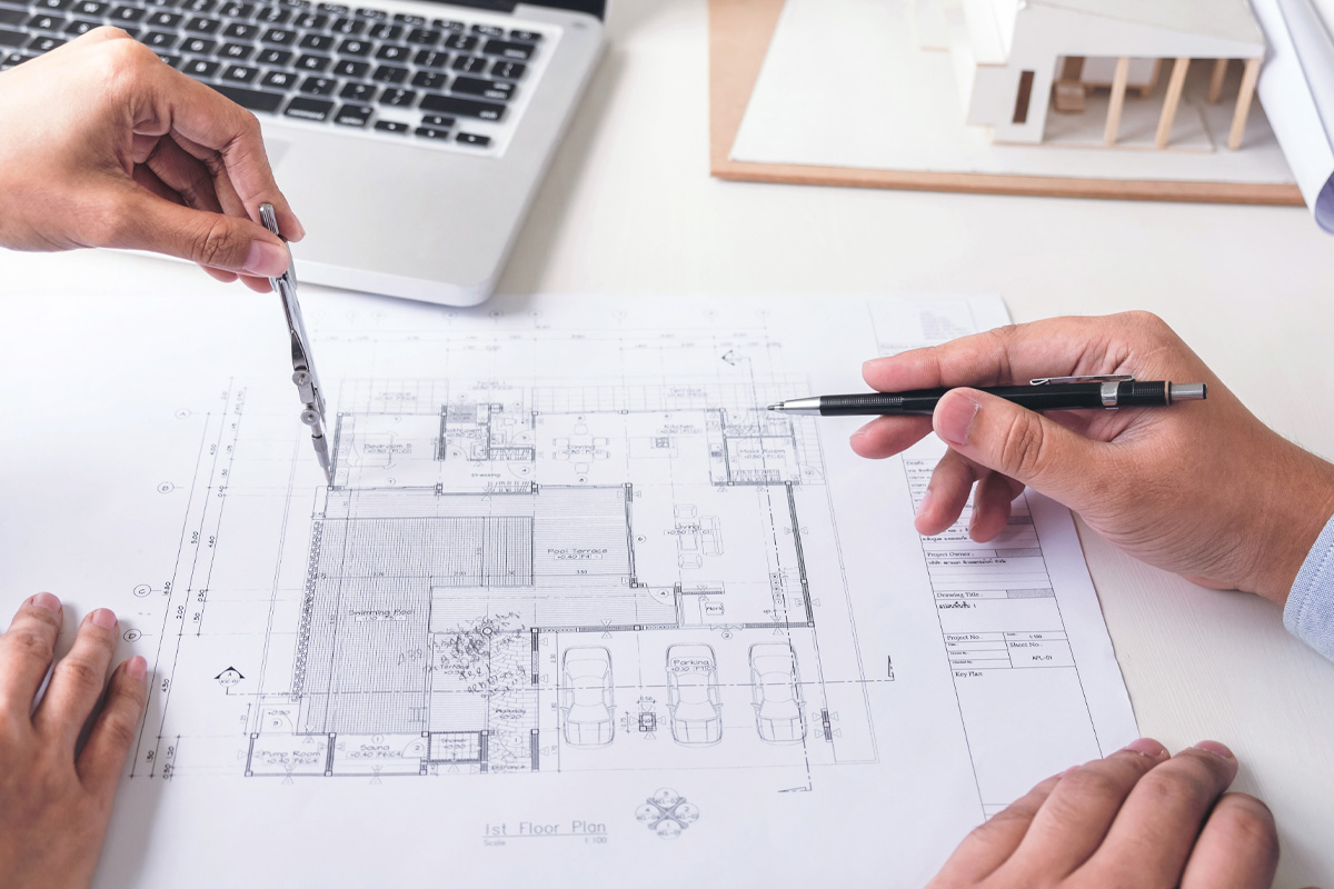 Two people reviewing architectural blueprints with a model house and laptop on the table, focusing on floor plans with pens in hand, consulting with construction dispute attorneys.