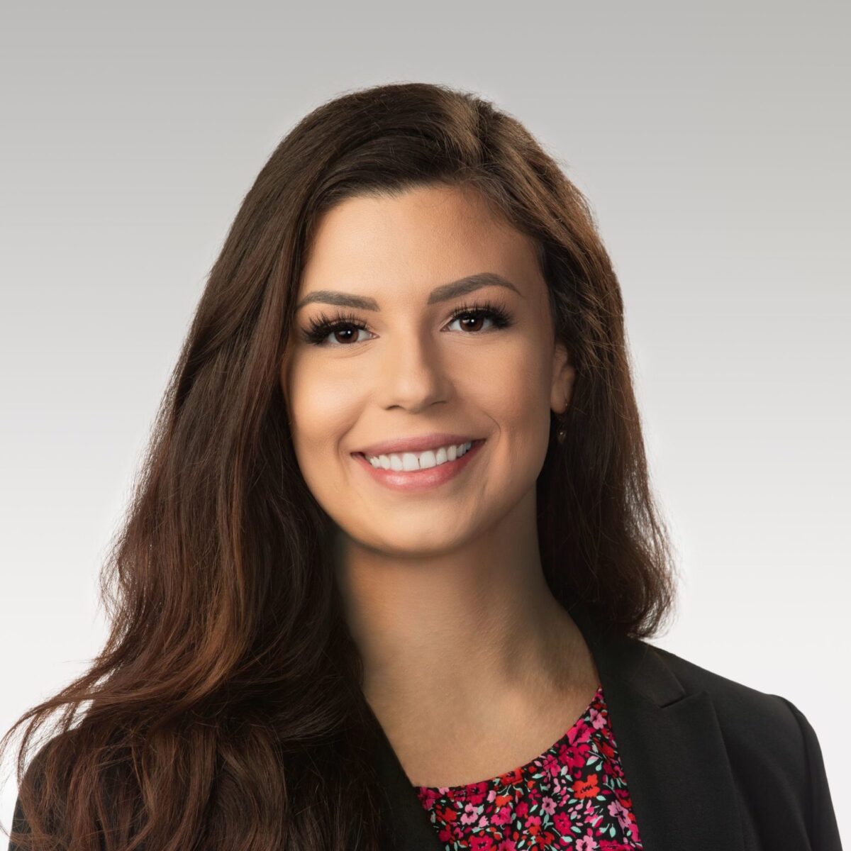 A professional headshot of Hannah S. Rullo, smiling with long brown hair, wearing a black blazer over a floral top, against a light gray background.