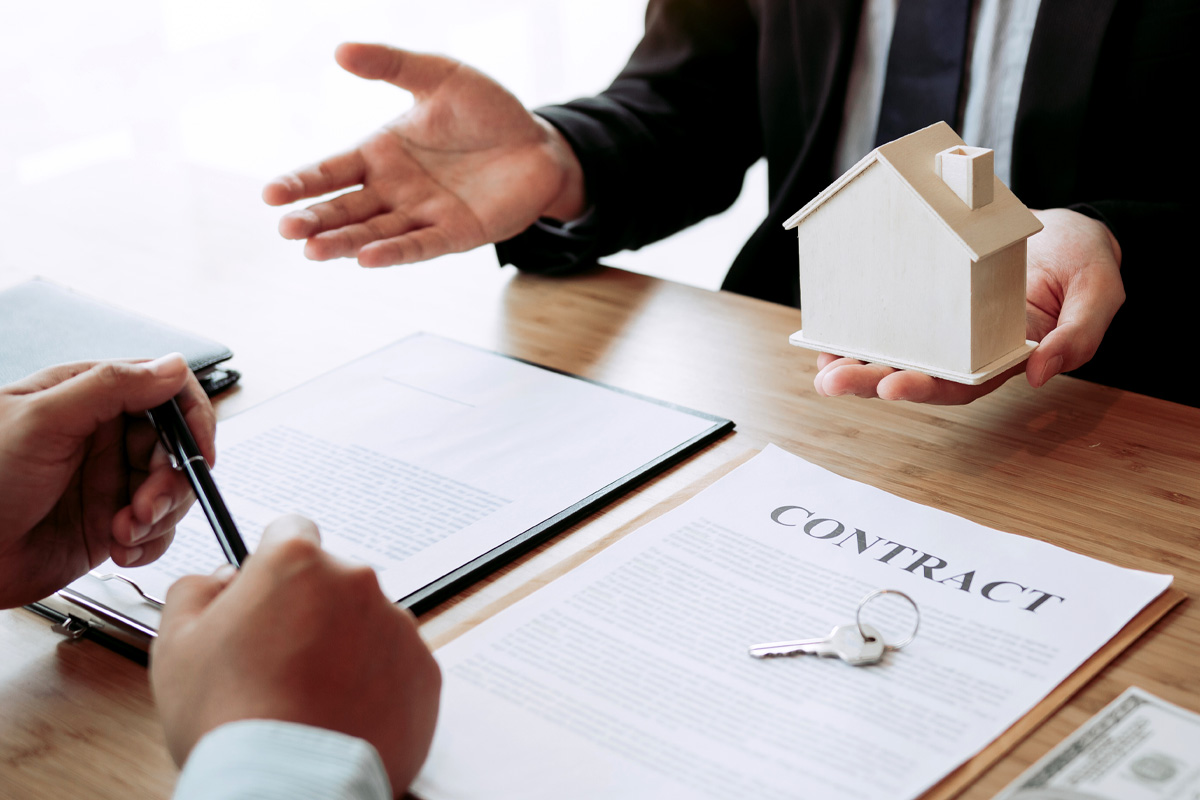 Two people in a business meeting, one holding a model house and another reviewing a contract, with a house key and money on the table, discussing landlord-tenant disputes.