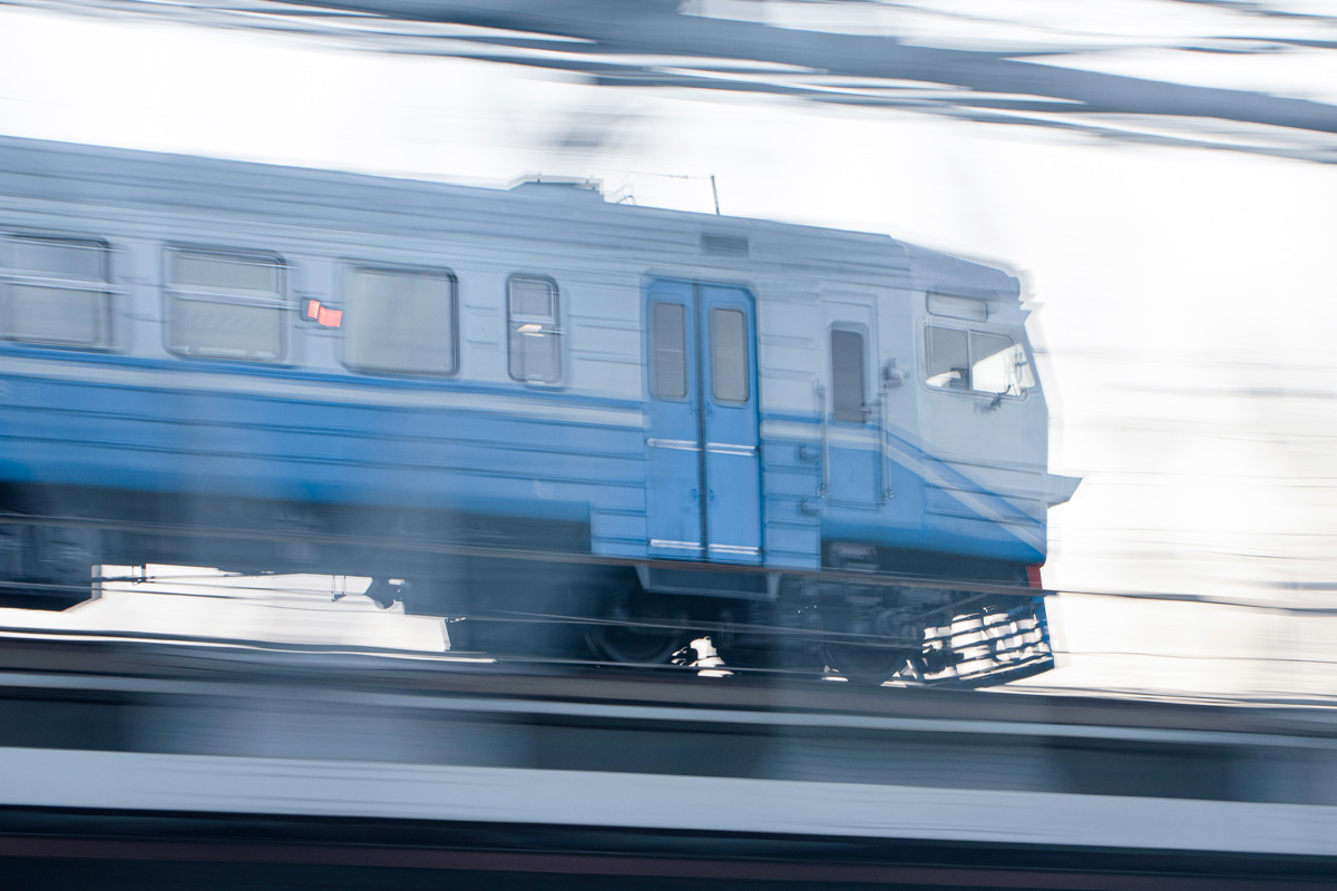 A blue train moving at high speed, captured with motion blur against a blurred background, emphasizing the sense of speed and movement in mass transit.