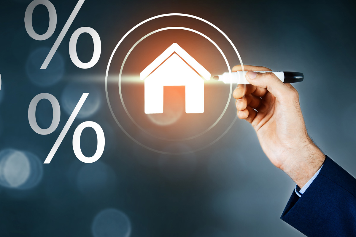 A man's hand holding a magnifying glass over a digital icon of a house surrounded by percentage symbols, symbolizing real estate brokers analyzing mortgage rates.