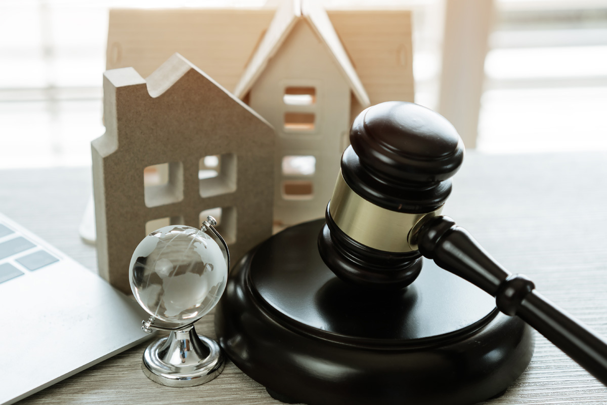 A wooden gavel and a small globe on a desk next to cardboard house models and a laptop, suggesting a theme related to real estate dispute litigation.
