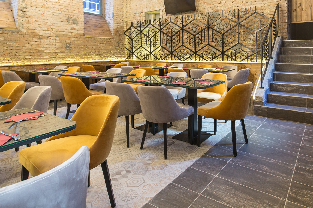 Interior of a stylish restaurant featuring eclectic velvet chairs in mustard and gray, decorative tables, and ornamental metal screens, with warm lighting and brick walls. Ideal for meetings with restaurant accident attorneys.