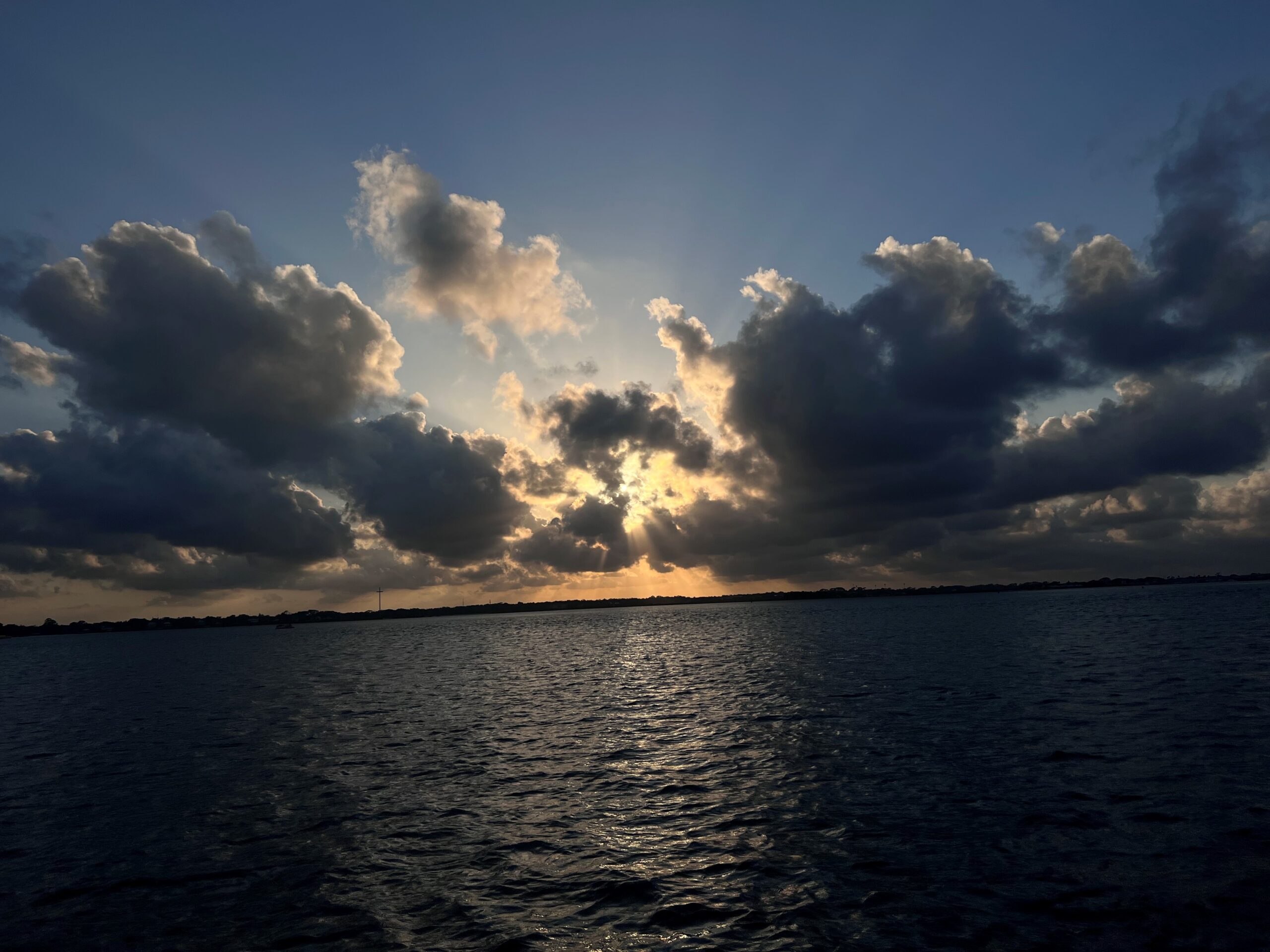 Sunset over a body of water in St. Augustine with dramatic cloud formations, the sun peeking through, casting a golden glow on the water.