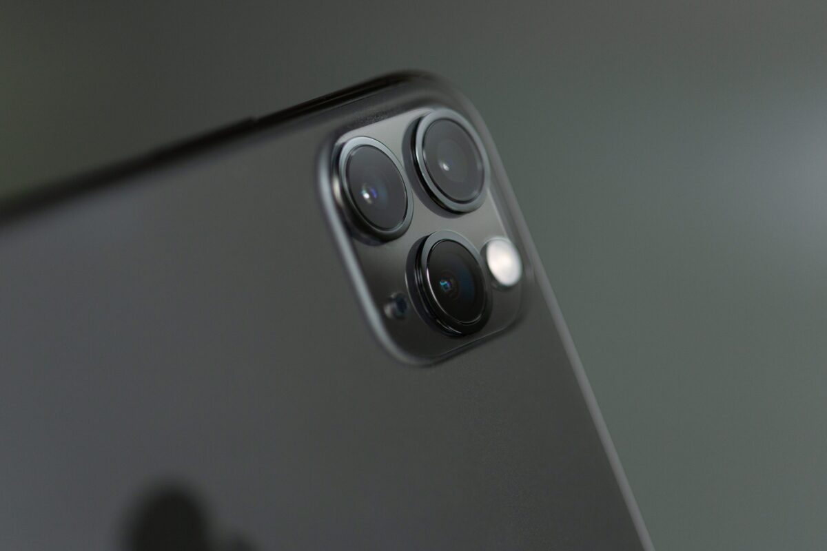 Close-up of a smartphone's rear camera system featuring three lenses, used to photograph a car crash, on a gray background.