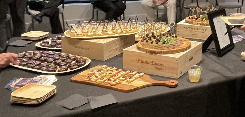A variety of gourmet appetizers displayed on wooden boards and crates at the Grand Opening catered event. Assortments include fruit tarts, canapés, and chocolate desserts.