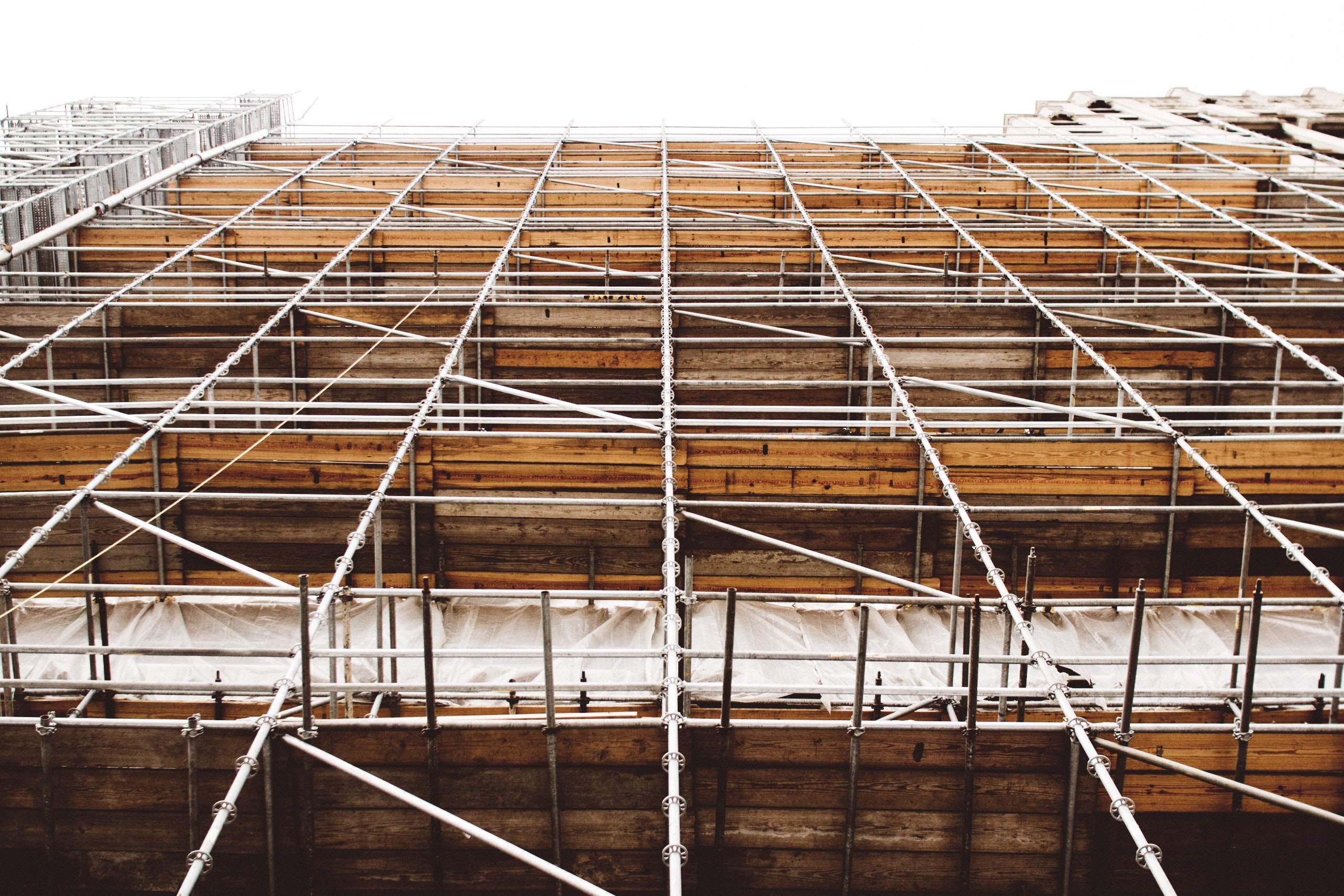 A view looking up at a building under construction reveals a complex network of metal scaffolding and wooden planks against a bright sky, a reminder of the importance of safety to prevent scaffolding accidents.