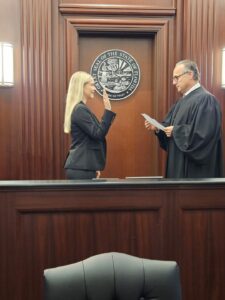 A woman stands in front of a judge, raising her right hand as if taking an oath, in a courtroom with the Florida state seal on the wall behind them.