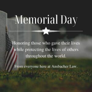 Memorial Day message on a blurred cemetery background with an American flag by a gravestone, honoring those who gave their lives protecting others. Text from Ansbacher Law.