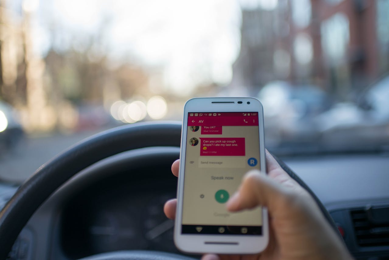 A person texting while driving, holding a smartphone in the driver’s seat, with the messaging app displayed and the steering wheel visible—highlighting the risky behavior that can lead to a car accident or being labeled an at-fault driver.
