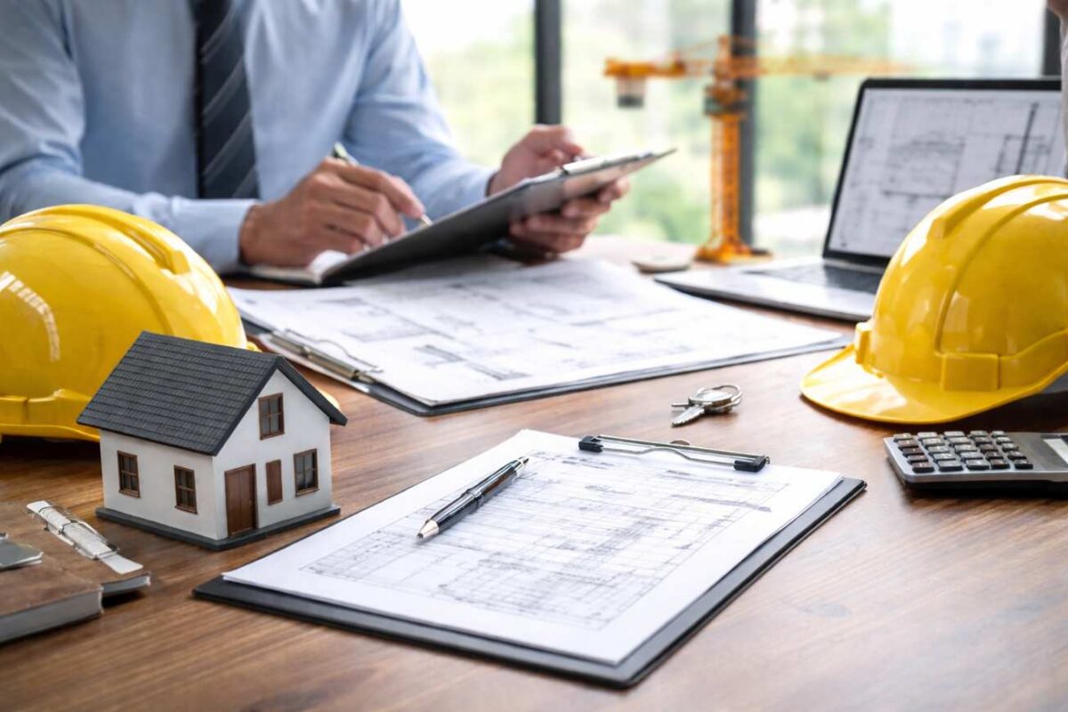 A person in business attire reviews documents at a desk with blueprints, a model house, yellow construction helmets, keys, and a calculator—reflecting the process of securing construction financing from banks in Florida; a model crane is visible in the background.