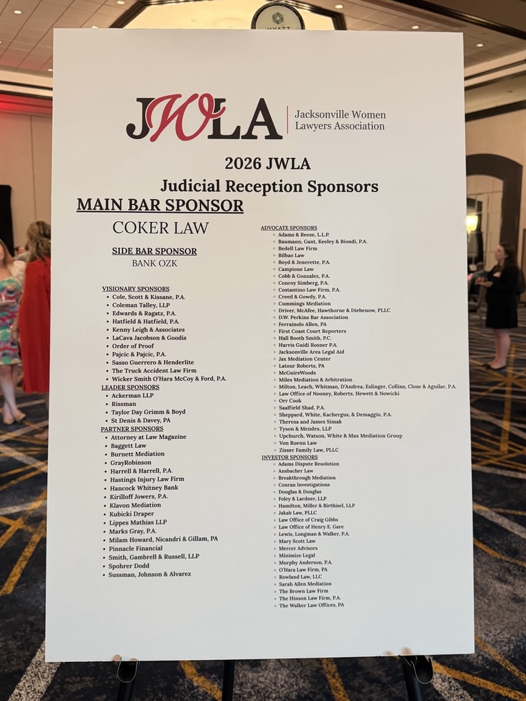 A large white sign lists sponsors for the 2026 Jacksonville Women Lawyers Association Judicial Reception, including Ansbacher Law Attorneys among main and side bar sponsors, visionary sponsors, and associate sponsors, displayed in a hotel event room.